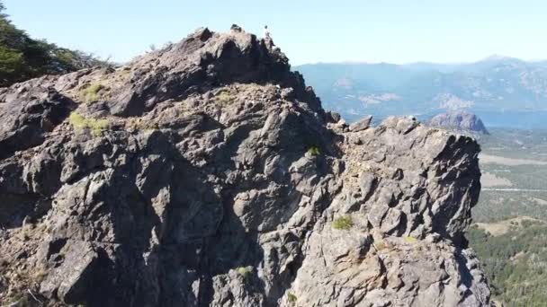 Voar aéreo em direção ao jovem no cume da montanha rochosa observando paisagem de lagos e cadeias de montanhas. Da frente panorâmica à vista superior.Paralaxe. San Martin de los Andes, Neuquen, Argentina — Vídeo de Stock