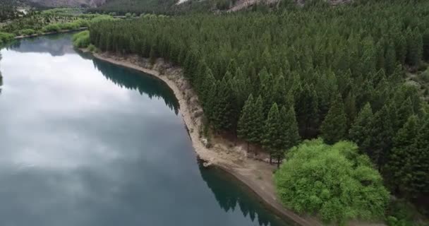 空中飞越纯蓝的水面沿着松树林海岸线飞行.背景是野生的山地山谷.自然景观。氧化铝河。阿根廷巴里洛切Valle Encantado — 图库视频影像