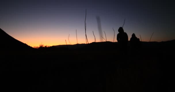 Silueta turistů kráčejících za úsvitu. Detail mladých mužů stoupajících po oranžovém pozadí. Omezená scéna. Tráva v popředí. Patagonia, Argentina — Stock video