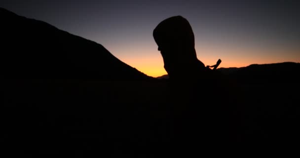 Napkeltekor sétáló fiatalember sziluettje. Fekete előtér és narancs háttér. Trekking a hegyvidéki táj. Patagónia. — Stock videók