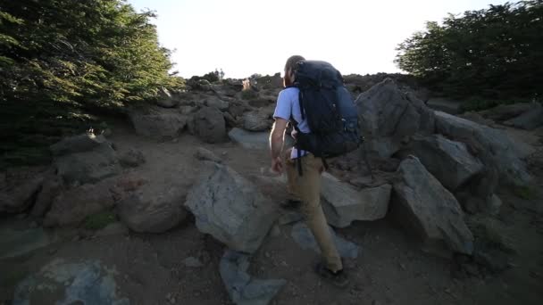 Scène au ralenti de jeune homme avec sac à dos randonnée montagne, rayons de soleil apparaissant derrière la personne tout en escaladant des rochers. Paysage sauvage, sentier vers Cerro colorado. Patagonie, Argentine — Video