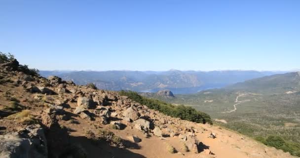 Trekking, ner för bergstoppen. Klippiga och kala markspår. Panoramautsikt över sjö, väg och skog. Vulkaniska, Cerro Colorado. Lanin nationalpark. San Martin de los Andes, Argentina — Stockvideo