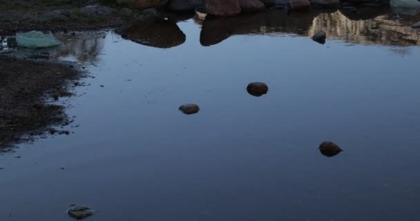 Női tükörkép a víz felett. A part sziklái és homokja. A meredek mozgás torzítja a képet. — Stock videók