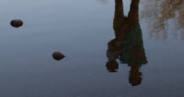 Suda el sallayarak veda eden kadın ve bebeğin yansıması. Dalgalanma hareketi görüntü bozulmasına neden olur. Rüya gibi, sürrealizm sahnesi.