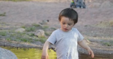 Bir yıl bebek doğada su ve kayaların üzerinde yürüdü. Su yansıması ile aydınlatılmış. Doğada tecrübe edinmek.