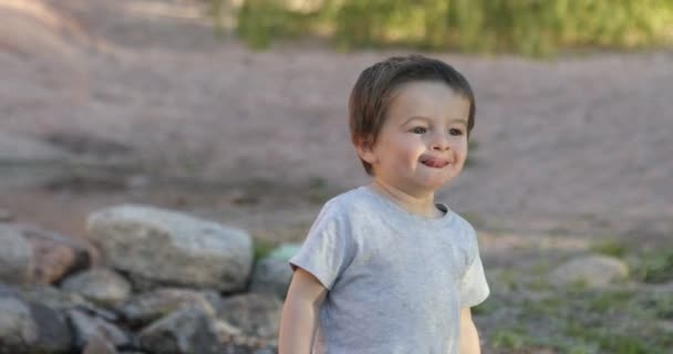 One year baby making funny faces, kisses and talking while he walks between rocks. Iluminated with the water reflection. Learning experience in nature. — Stock Video