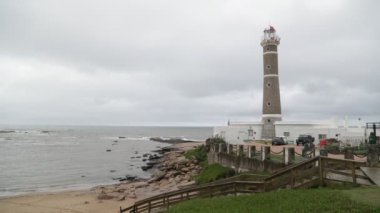 Kayalık ve kumlu sahil şeridinde deniz feneri. Sahile giden ağaçtan merdiven boşluğunda. Bulutlu bir gün. Jose Ignacio, Rocha, Uruguay