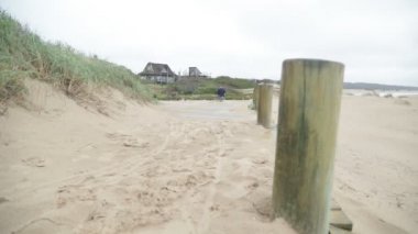 Sahildeki ahşap patika boyunca yürüyen bir çocuğun yavaş çekim sahnesi. Arka planda San Kum tepeleri. Jose Ignacio, Rocha, Uruguay