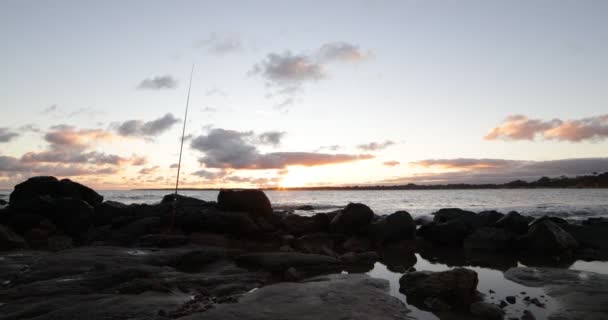 黄金の時間でビーチのスローモーション。波が砂でブレーキしながら海岸線や釣竿で岩の前景。海面上の黄金の反射。地平線の夕日。ウルグアイのピリオポリス — ストック動画