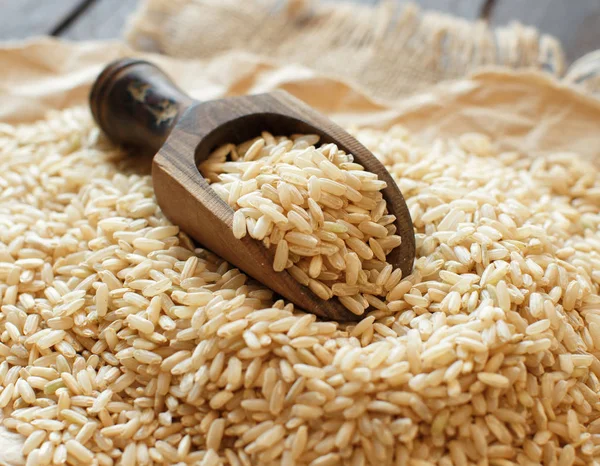 Hromadu hnědá rýže s dřevěnou lžící — Stock fotografie