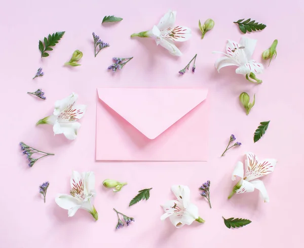 Flores e envelope em um fundo rosa claro — Fotografia de Stock