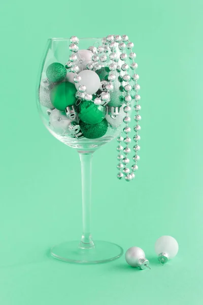 Christmas baubles in a wine glass on a light green background — Stock Photo, Image