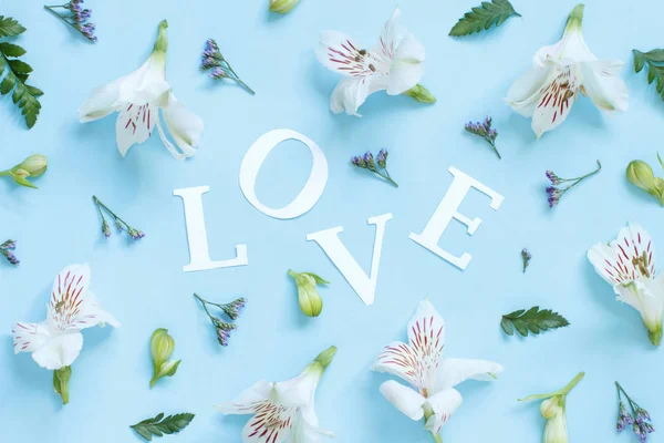 Flores, pétalas e palavra Amor sobre um fundo azul claro — Fotografia de Stock