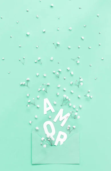 Flores, envelope e texto AMOR em um fundo verde claro — Fotografia de Stock