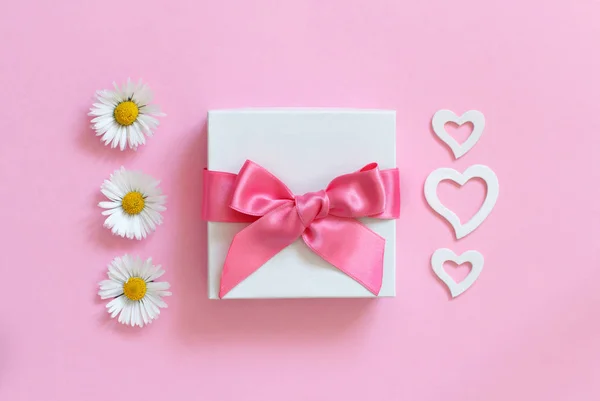 Caixa de presente branco, margaridas e corações em um fundo rosa claro — Fotografia de Stock