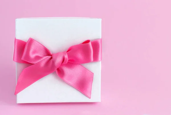 Белая подарочная коробка с бантом на светло-розовом фоне — стоковое фото
