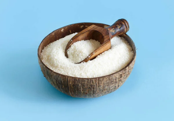 Harina de coco en un tazón con una cuchara sobre un fondo azul claro —  Fotos de Stock