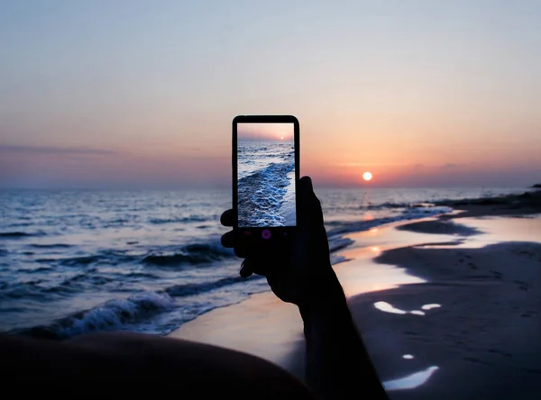 男は携帯電話で夕日の写真を撮っている — ストック写真