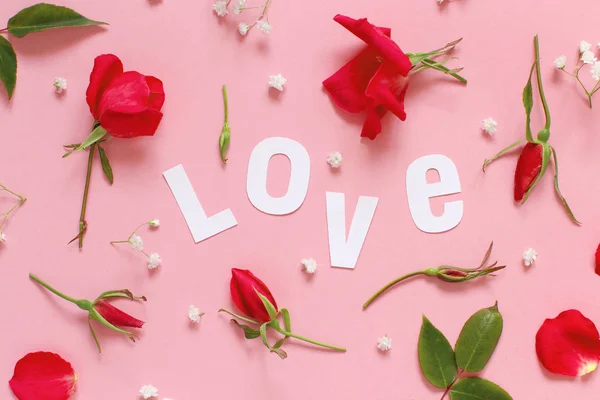 Rosas vermelhas e texto AMOR em um fundo rosa claro — Fotografia de Stock