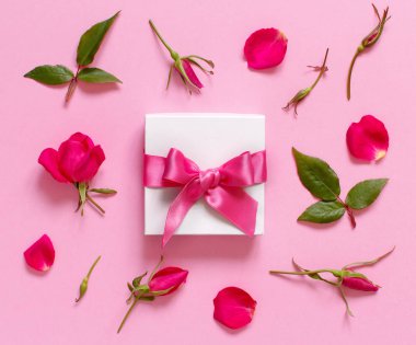 Açık pembe arka planda beyaz hediye kutusu ve çiçekler.