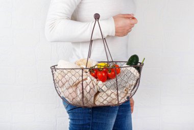 Kadınlar taze sebzelerle dolu bir sepet ve tekstil torbaları bulundururlar.