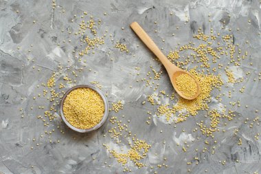 Gri arka planda kaşık üst görüşü olan bir kasede kurumuş darı var.