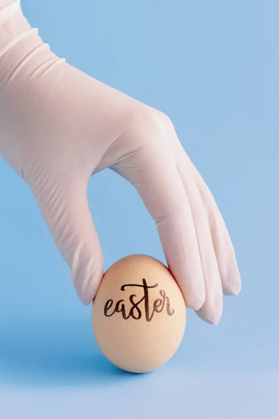 Mano Nel Guanto Mantenendo Uovo Con Iscrizione Pasqua Sfondo Blu — Foto Stock