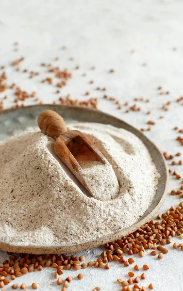Buckwheat flour in a plate with a spoon and buckwheat grain close up