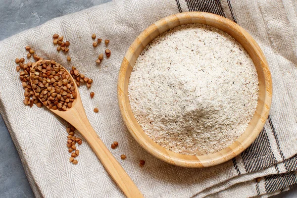 Buckwheat flour in a bowl and buckwheat grain in a spoon top view