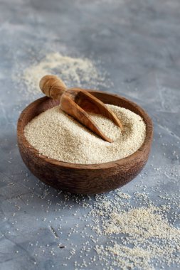 Çiğ, pişmemiş fonio tohumları bir kasede, arka planda gri bir kaşık ve fotokopi alanı var.