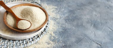 Çiğ pişmemiş fonio tohumları ve gri arkaplanda bir kaşık fotokopi alanı ile yakın plan