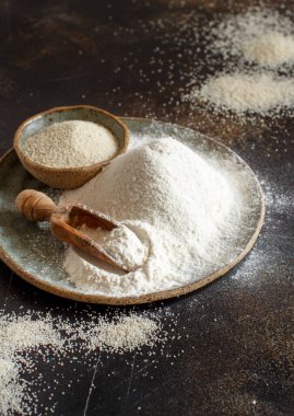 Çiğ fonio unu ve tohumlar bir tabakta koyu arka planda kaşıkla yakın plan. Alternatif un