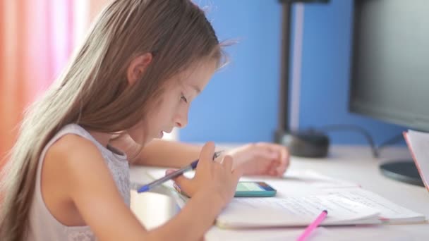 Menina estudante fazendo lição de casa. A rapariga aprende lições. usando smartphone — Vídeo de Stock