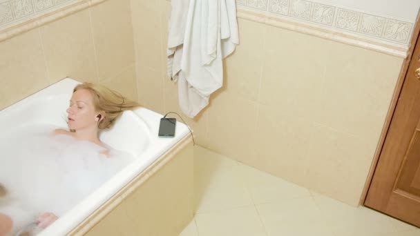 Belle femme prenant un bain et écoutant de la musique sur écouteurs. téléphone portable — Video