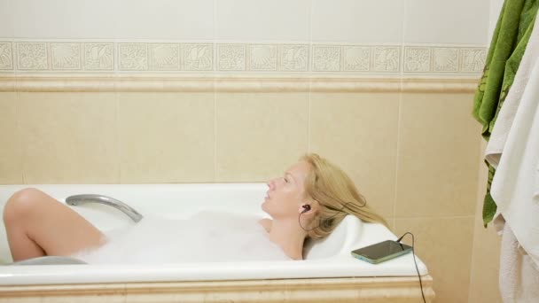 Belle femme prenant un bain et écoutant de la musique sur écouteurs. téléphone portable — Video