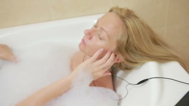 Hermosa mujer tomando un baño y escuchando música en los auriculares. teléfono celular — Vídeo de stock