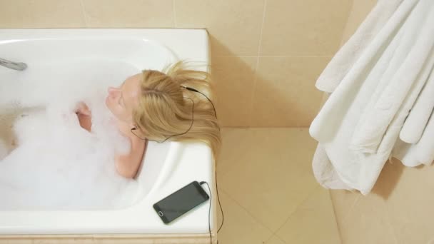 Bela mulher tomando um banho e ouvir música em fones de ouvido. telefone celular — Vídeo de Stock