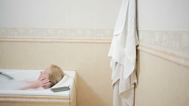 Beautiful woman taking a bath and listening to music on headphones. cell phone — Stock Video