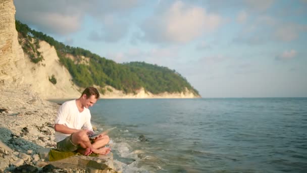 Счастливый человек с современным ноутбуком сидит на пляже. удаленная работа — стоковое видео