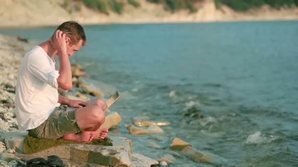 Uomo felice con computer portatile moderno seduto sulla spiaggia. lavoro a distanza — Video Stock