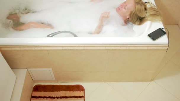 美丽的女人洗个澡，在耳机上听音乐。手机 — 图库视频影像