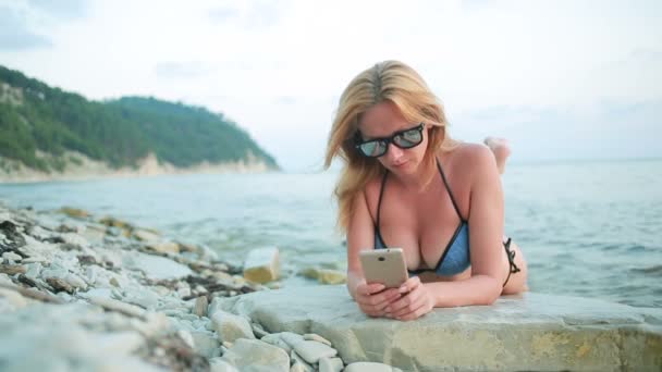 Mädchen am Strand mit einem Smartphone. sexy Frau im Bikini — Stockvideo