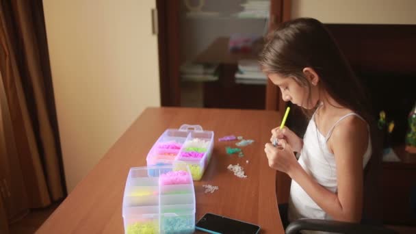 Niña teje pulsera de bandas elásticas. Bandas de goma de colores para tejer — Vídeo de stock