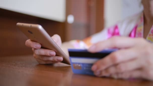 Mujer hace una compra usando un teléfono inteligente y una tarjeta bancaria . — Vídeo de stock