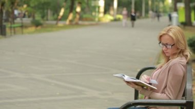 sarışın kadın okuma kitabı Brench sonbahar Park üzerinde. sıcak kahve veya çay içme