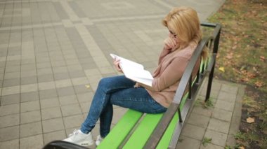 sarışın kadın okuma kitabı Brench sonbahar Park üzerinde.