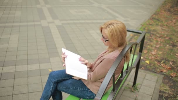 Szőke nő olvasókönyv a fogorvostudomány őszi parkban. — Stock videók