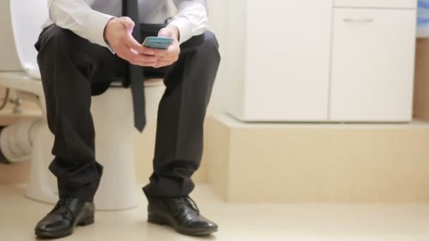 Male businessman watches the news on the phone sitting on the toilet — Stock Video