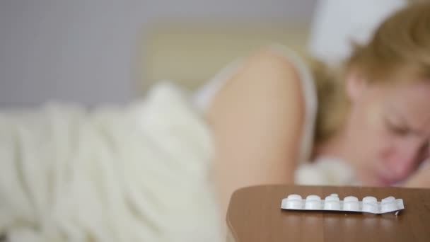 Хвора жінка лежить на ліжку. таблетки і склянку води. пити таблетки. знеболюючий засіб — стокове відео
