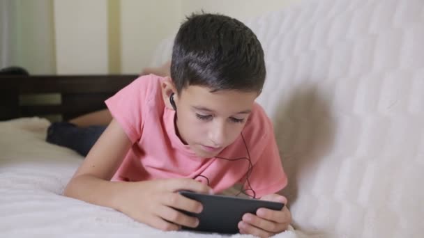 Niño con smartphone y auriculares escuchando música o jugando en casa — Vídeos de Stock